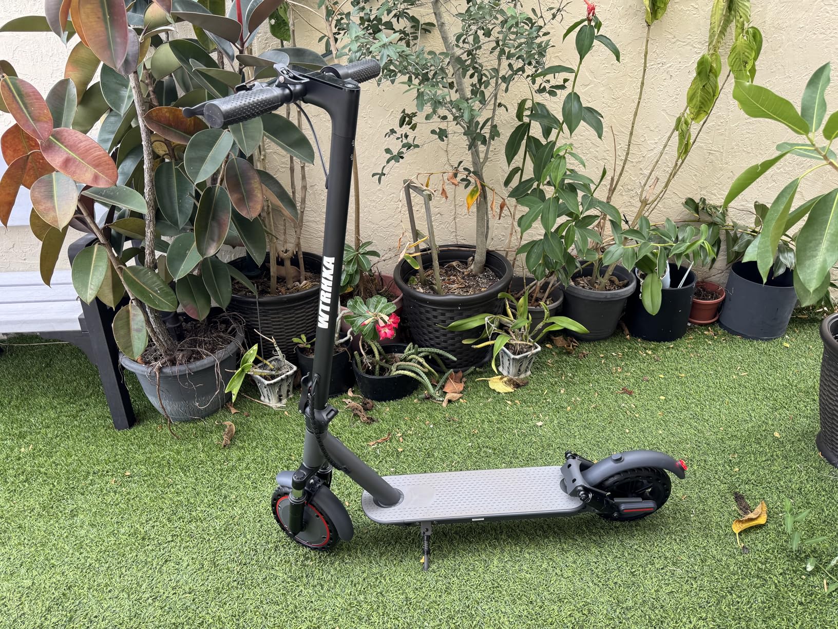 Black WTRHXA electric scooter with red wheel trim parked on artificial grass in a patio garden