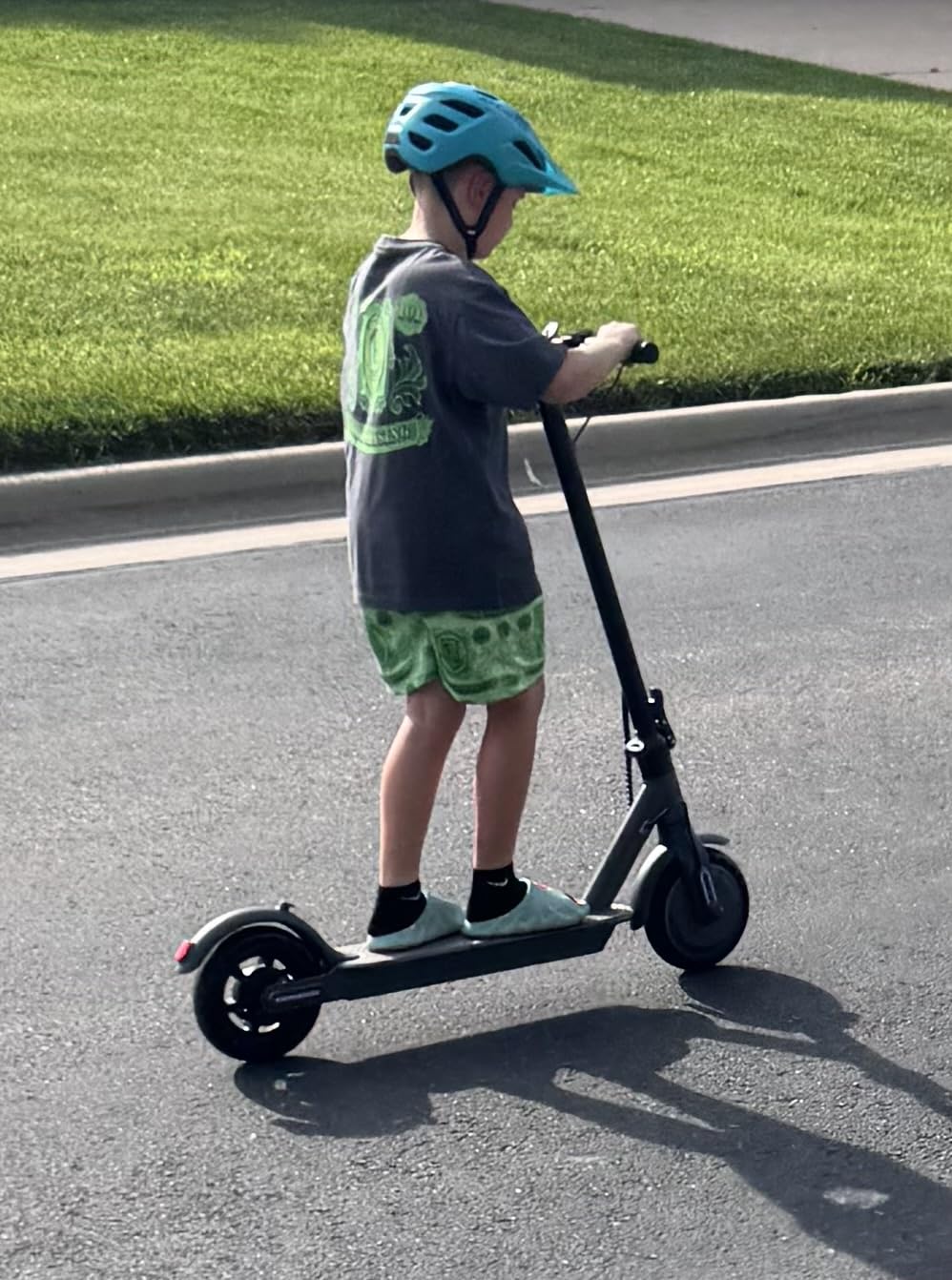 Kid in a blue helmet riding a WTRHXA electric scooter down a driveway
